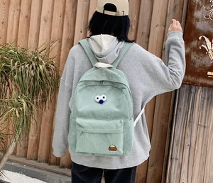 Close-up of light green corduroy backpack with cartoon eye embroidery worn by model