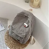 Detail of gray corduroy backpack featuring fun cartoon eye patches on a woven mat