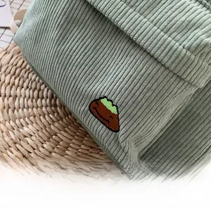 Close-up of light green corduroy backpack showing texture and cute mountain embroidery