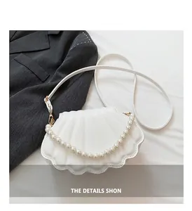 Detalle de bolso de concha blanca con herrajes dorados y asa de perlas imitación
