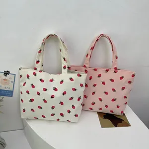 Detailed close-up of corduroy tote bags with strawberry print in cream and pink