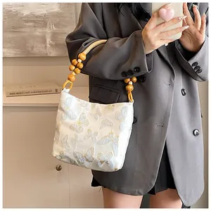 Détail de la poignée en perles de bois et broderie papillon sur un sac sous le bras