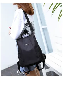 Side view of a black anti-theft nylon backpack worn by a model in a minimalist setting