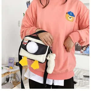 Dettaglio borsa a tracolla con pon-pon bianchi e decorazione a forma di zampe di papera