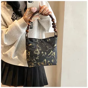 Détail de la broderie papillon dorée et de la poignée en perles de bois du sac noir