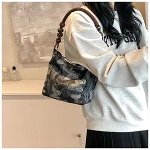 Détail de la bandoulière en perles de bois et broderie papillon sur sac gris