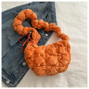 Close-up of bright orange quilted plush shoulder bag with bubble texture on denim background