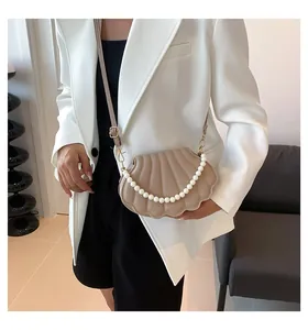 Elegante bolso concha beige con asa de perlas y textura grabada sobre una modelo