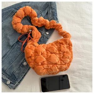 Close-up of orange plush ruched shoulder bag with quilted texture on denim background