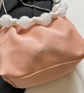 Detalle del bolso nube rosa con asa de cuentas blancas y logotipo plateado fashion