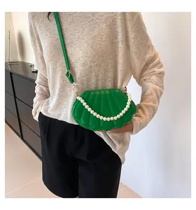 Detalle del bolso bandolera verde con forma de concha y elegante asa de cadena de perlas