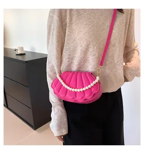 Detalle de bolso bandolera de concha rosa con textura 3D y cadena de perlas