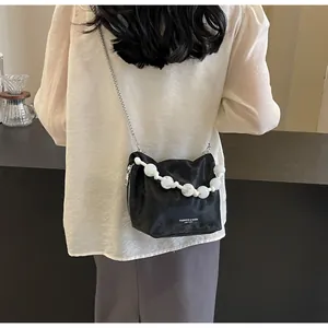 Bolso tipo cubo negro con asa de perlas y correa de cadena mostrado en un modelo