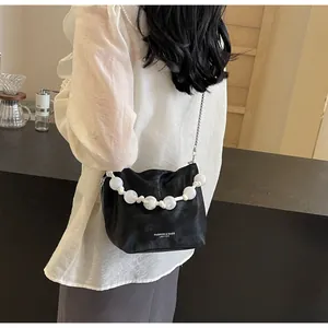 Detalle de bolso plisado negro con asa de perlas blancas y correa de cadena plateada