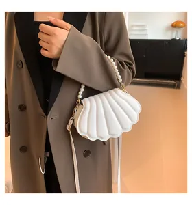 Detalle de bolso de concha blanca con asa de perlas y textura acolchada sobre gabardina