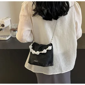 Detalle de bolso bandolera negro con asa de perlas blancas y letras de cuero de moda