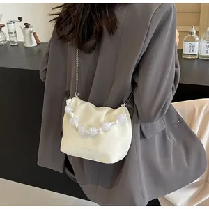 Detalle de bolso cubo plisado crema con asa de perlas grandes y cadena metálica fina