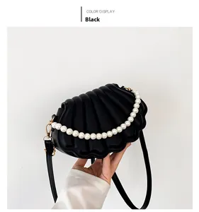 Detalle de bolso bandolera negro con forma de concha, cadena de perlas y correa