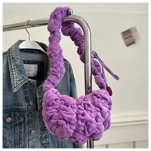 Detail view of purple pleated cloud bag hanging on metal rack with denim jacket background