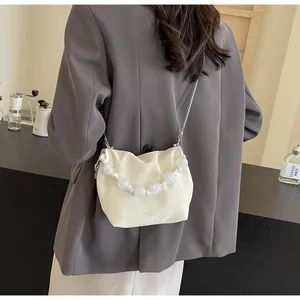 Detalle del bolso tipo cubo de cuero plisado beige con asa de grandes cuentas blancas