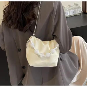 Detalle del bolso plisado crema con asa de perlas grandes y correa de cadena plateada