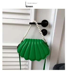 Detalle de bolso bandolera verde con forma de concha, asa de perlas y textura de cuero