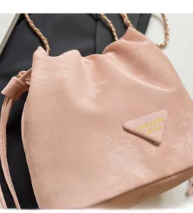 Gros plan du sac seau en daim rose avec bandoulière en chaîne dorée et logo latéral