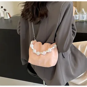 Detalle de bolso bucket de piel plisada rosa claro con asa de perlas blancas y cadena plata