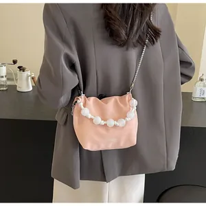 Detalle de bolso saco rosa con asa de cuentas blancas y correa de cadena plateada en un café