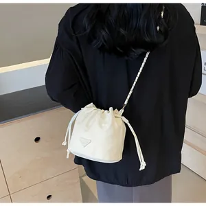 Détail d'un sac seau beige à cordon avec bandoulière chaîne porté par un mannequin chez soi