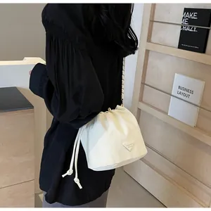 Détail du sac seau crème avec cordon de serrage, chaîne en métal et plaque logo