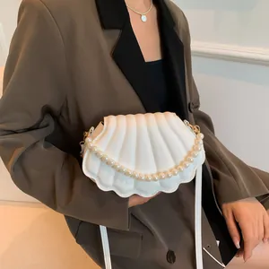 Bolso bandolera blanco con forma de concha y cadena de perlas puesto en modelo
