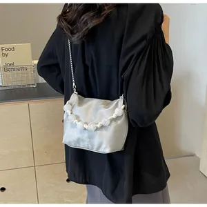 Bolso tipo cubo de satén plateado con asa de perlas y cadena metálica visto desde la espalda