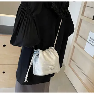 Sac seau argenté avec cordon de serrage, logo triangulaire et détail de bandoulière