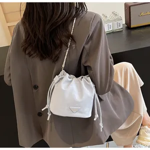 Détail du sac seau gris clair avec cordon de serrage et logo triangulaire sur le mannequin