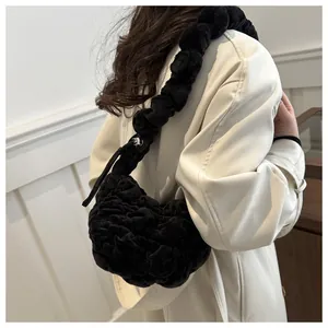 Close-up of black plush pleated cloud bag worn as a stylish shoulder bag on a beige coat