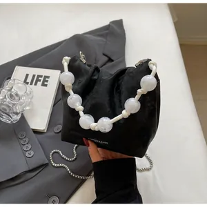 Detalle de bolso de cubo en terciopelo negro con asa de perlas blancas y cadena plata