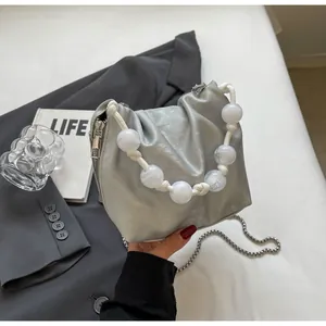 Detalle de bolso tipo saco plisado plateado con asa de perlas blancas y cadena metálica