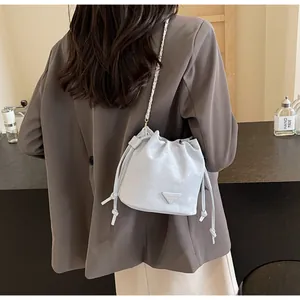 Détail d'un sac seau bleu clair à cordon avec une plaque logo triangulaire argentée