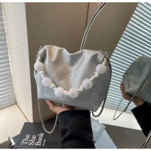 Vista detallada del bolso de mano plateado metalizado con cadena de perlas y logotipo