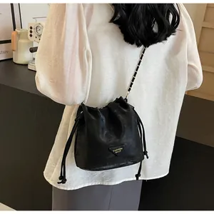Vue détaillée du sac seau noir à cordon avec bandoulière en chaîne dorée et plaque logo