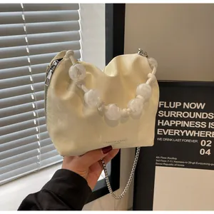Detalle de bolso crema con asa de cuentas transparentes y cadena metálica fina