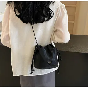 Détail d'un sac seau noir à cordon avec bandoulière dorée porté par un modèle