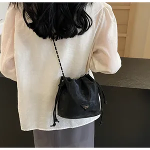 Détail d'un sac seau noir avec bandoulière chaîne dorée porté par un mannequin