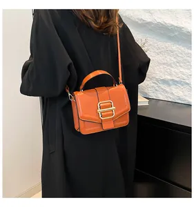 Burnt orange leather crossbody bag with gold buckle shown on a stylish black coat