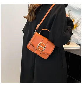 Detail of bright orange faux leather bag with large gold buckle and adjustable strap