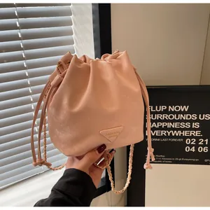 Gros plan d'un sac seau rose pâle avec bandoulière en chaîne dorée et texture cuir fin
