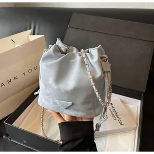 Détail du sac seau bleu clair avec bandoulière chaîne dorée dans un coffret cadeau