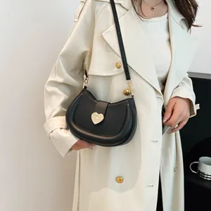 Sac à main demi-lune noir avec boucle coeur dorée porté sur un trench-coat beige élégant