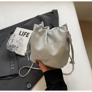 Vue détaillée du sac seau argenté métallisé avec cordon, chaîne et logo triangulaire